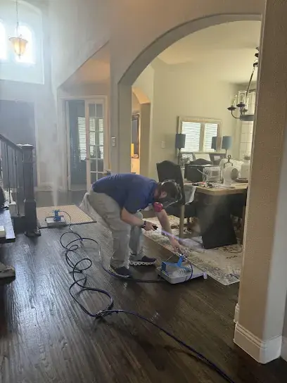 Technician setting up drying equipment and hoses on a wood floor under an arched entry in a Prosper, TX home