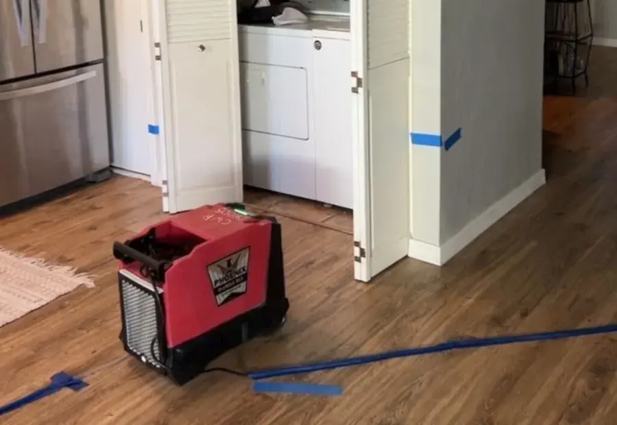 A dehumidifier on a wood floor outside a laundry closet, with tape on the floor marking the drying area