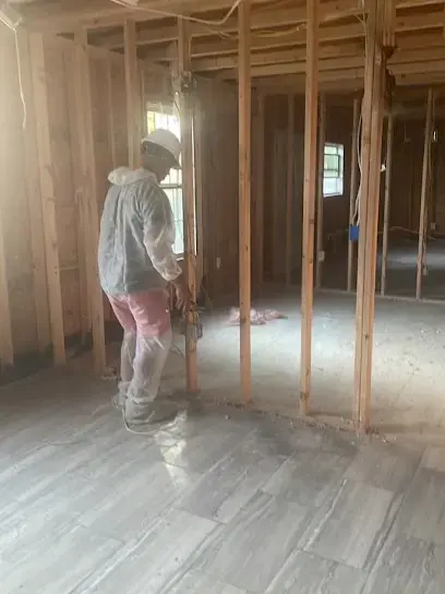 A technician in protective gear working in a room opened to the studs after water damage