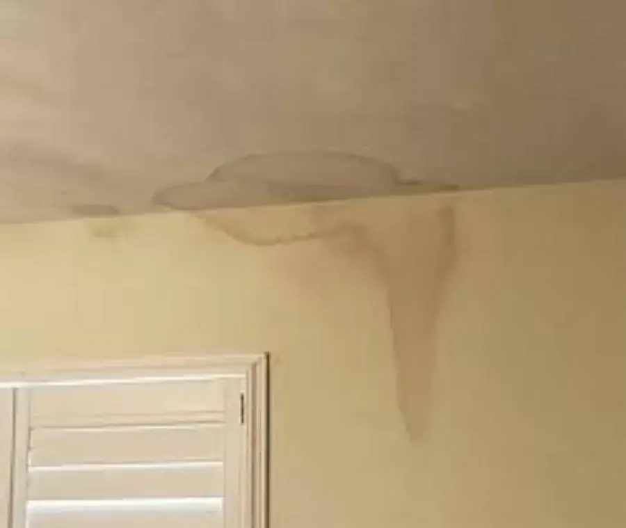 Water stain spreading across a ceiling and running down the wall beside a shuttered window in Prosper, TX