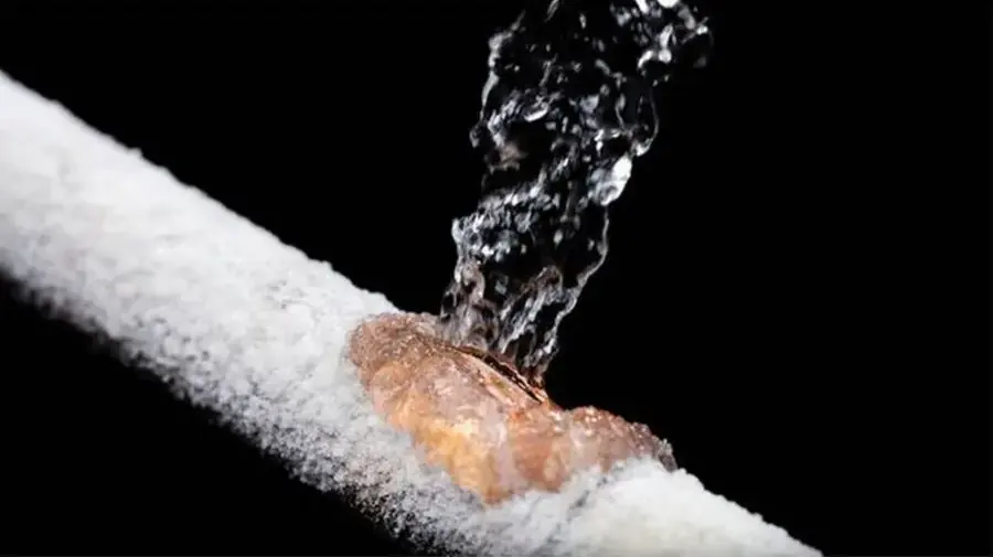 Ice-covered copper pipe split open and spraying water, the kind of frozen pipe failure Prosper, TX sees in a hard freeze