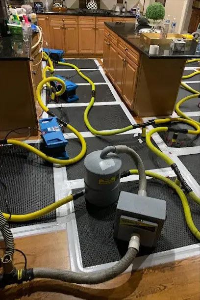Air movers and dehumidifiers set up to dry the floor and walls of a room in a Celina house.